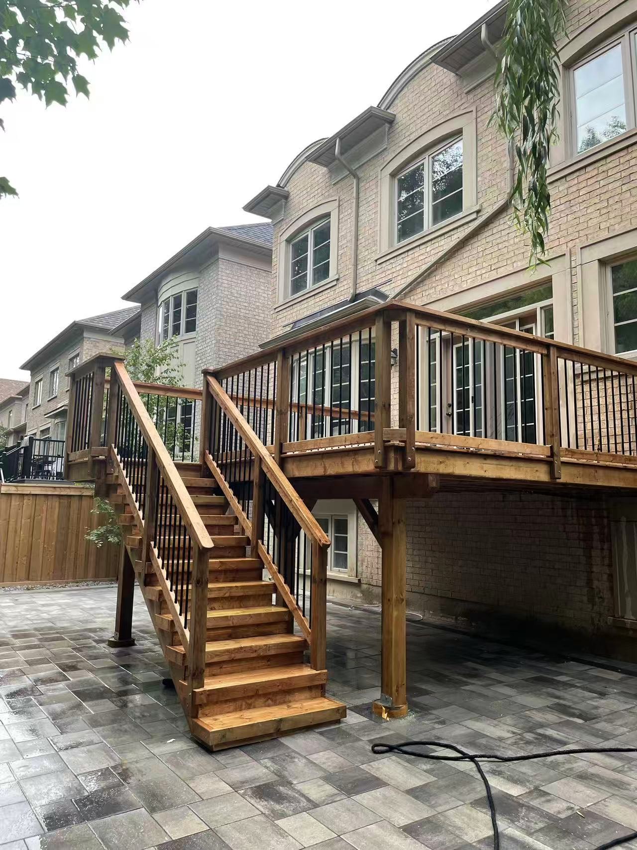 Elevated deck with black metal balusters and wood stairs over interlock patio